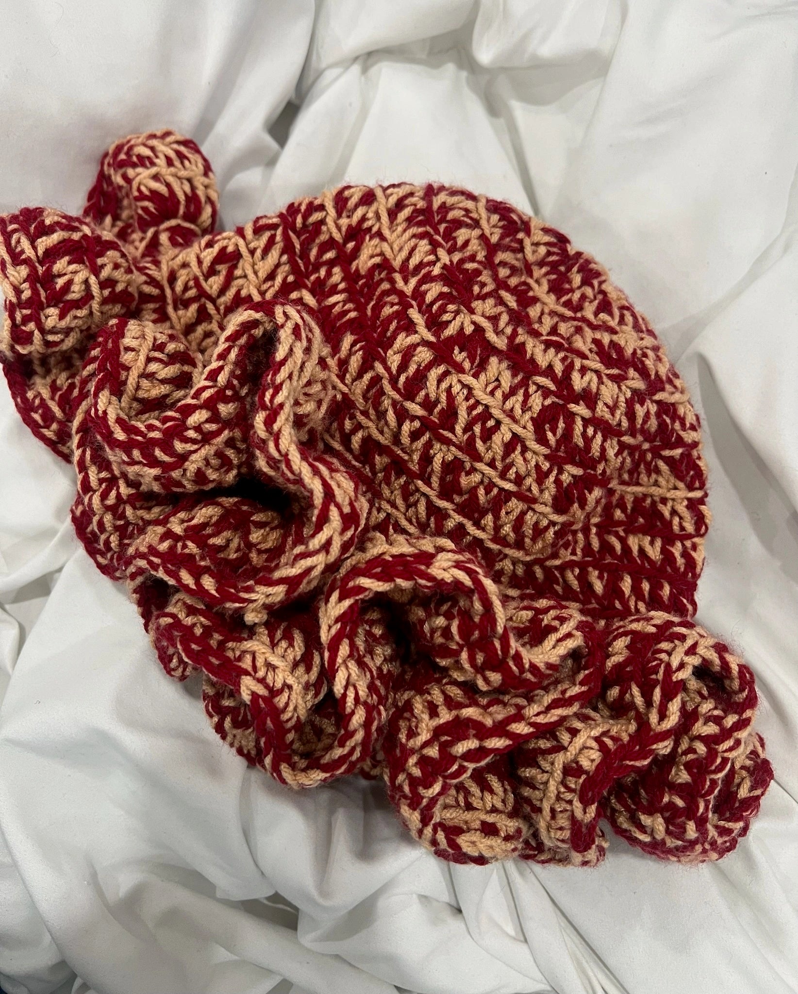 Crochet red and beige beanie on a white fabric background