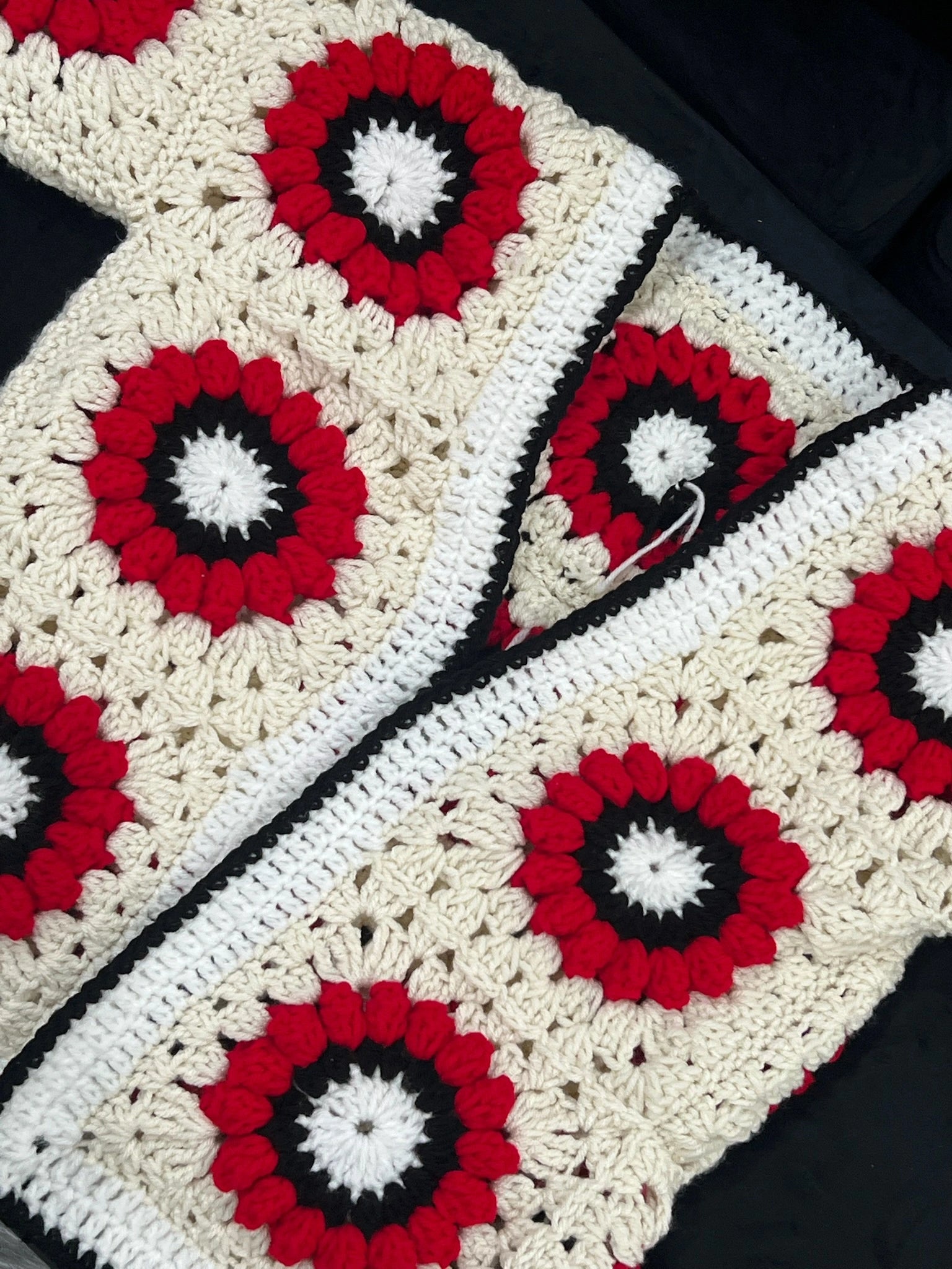 Crocheted cardigan with red, white, and black circular patterns on a dark background